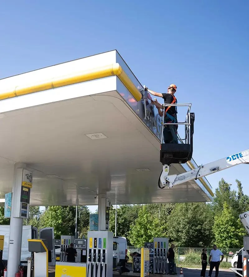 Technician using an aerial lift to work on gas canopy fascia at a fuel station