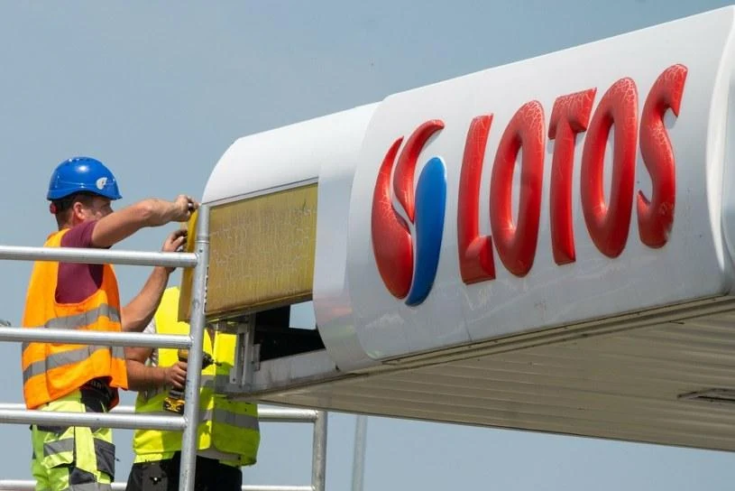 Technicians working on a LOTOS logo panel mounted on a gas canopy fascia